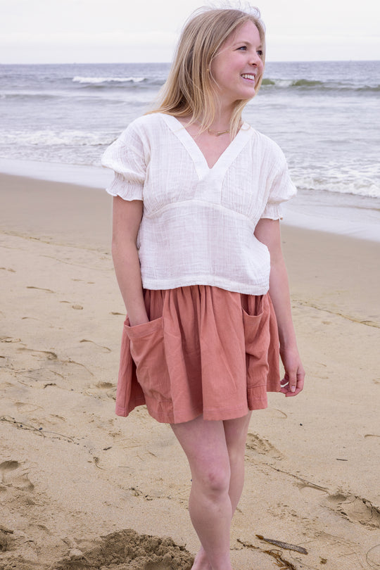 Woman on beach wearing mini skirt with pockets and white shirt.