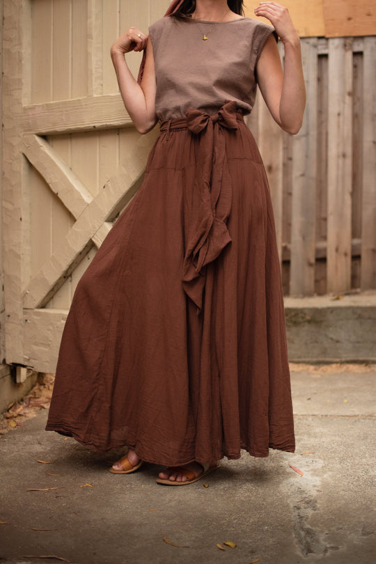 Model poses in brown shirt and long brown skirt with bow at waist.