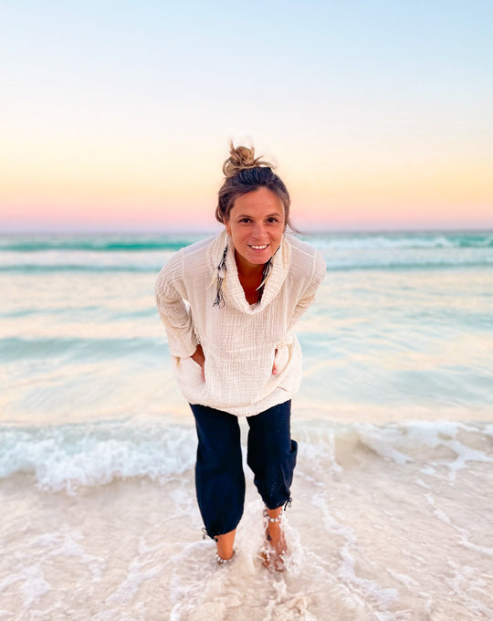 Model stands in ocean wearing white turtle neck sweater and navy pants.