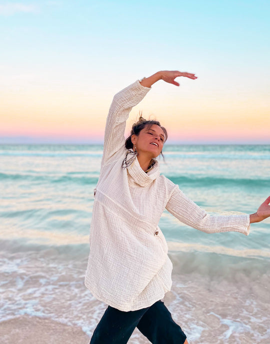 Female clothing model is dressed in natural white gauze shirt with cowl neck and navy pants.