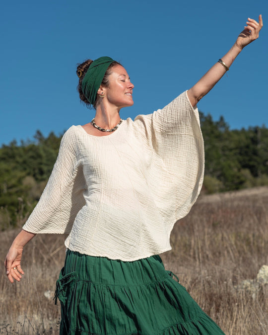 Woman wears pull over white top, green skirt and green head scarf. Shirt has wide sleeves.