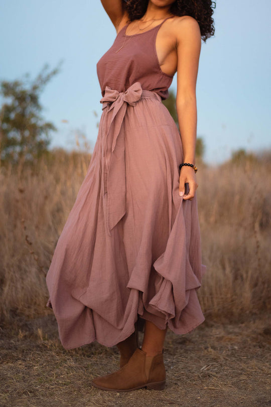 Model wears purple gauze tank top and long skirt with bow.